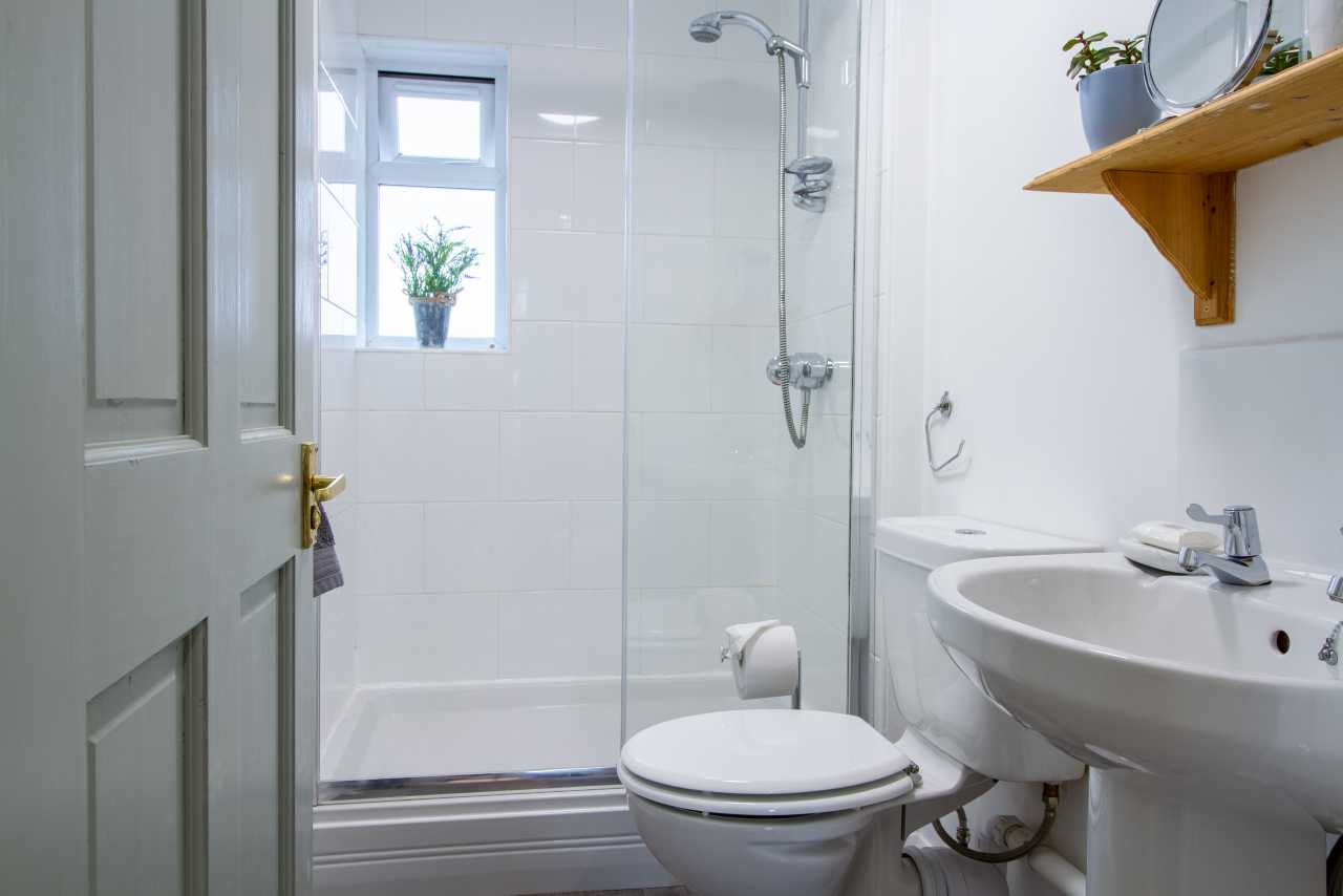 A bright bathroom with a bathtub and shower, toilet, pedestal sink, tiled walls, and a small window.