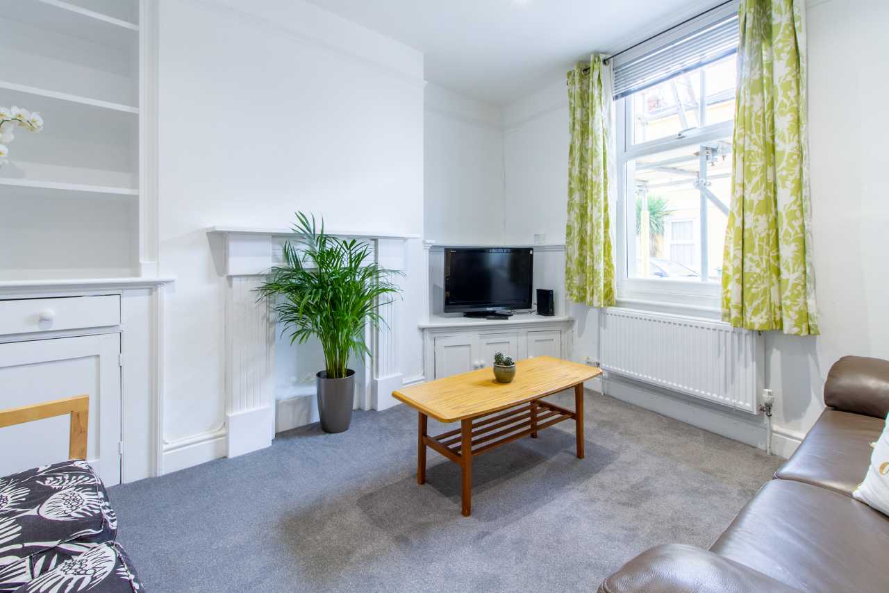 Bright furnished living room with a sofa, television, coffee table, fireplace and large window.