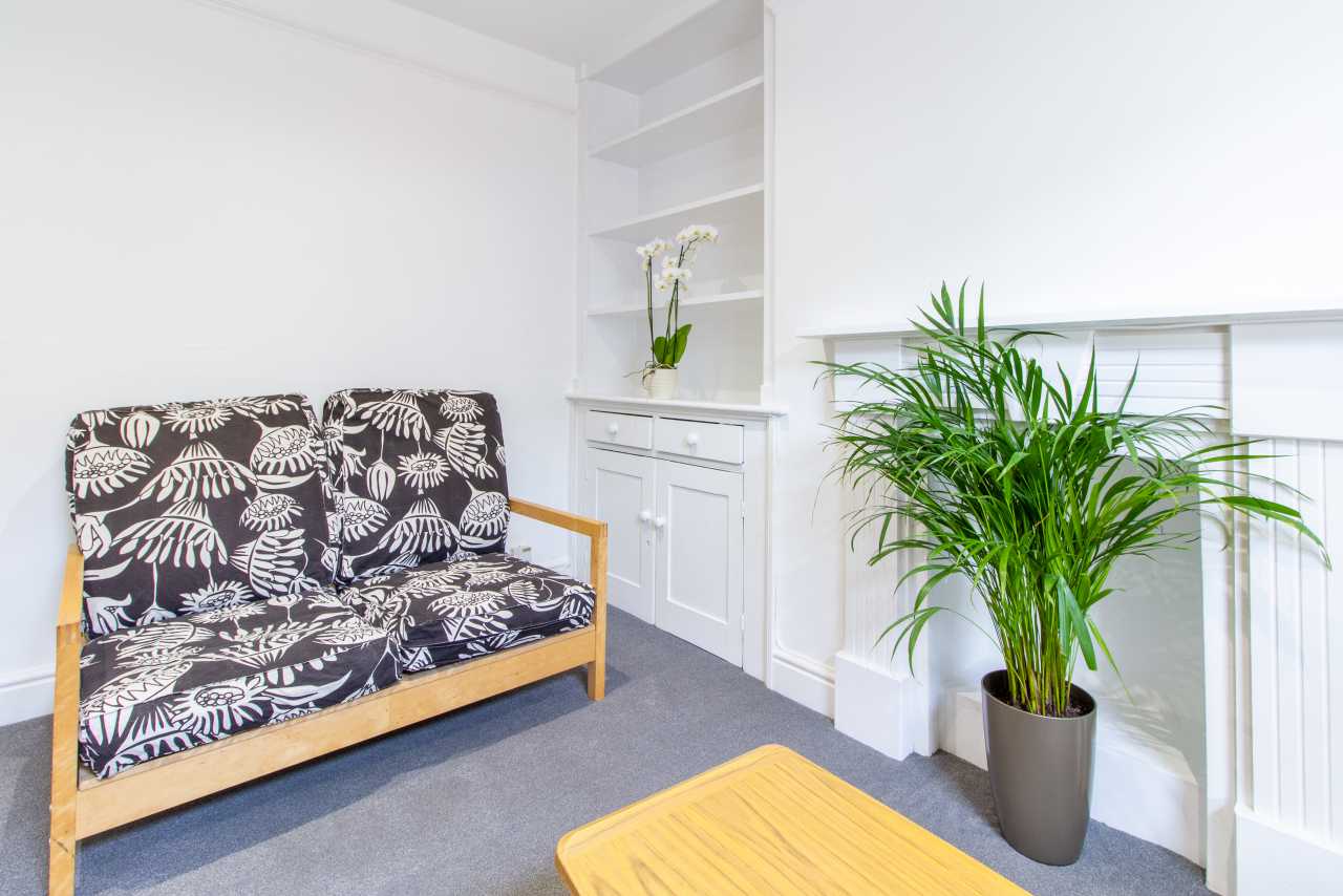 Bright sitting area with a patterned sofa, built-in shelving, a cabinet, a potted palm and a wooden coffee table.