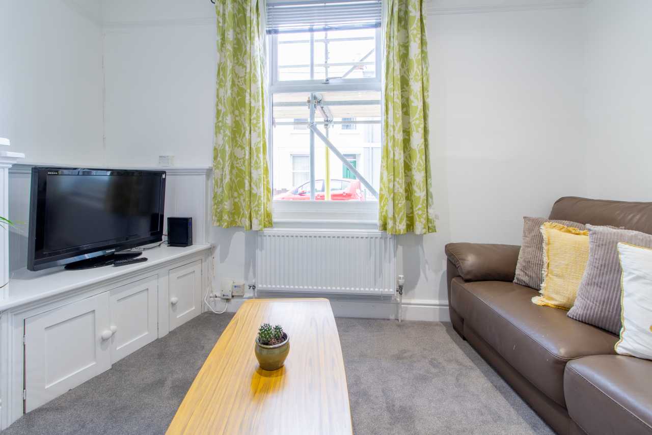 Bright living room with a television on a white cabinet, a brown sofa, coffee table, radiator and patterned curtains.