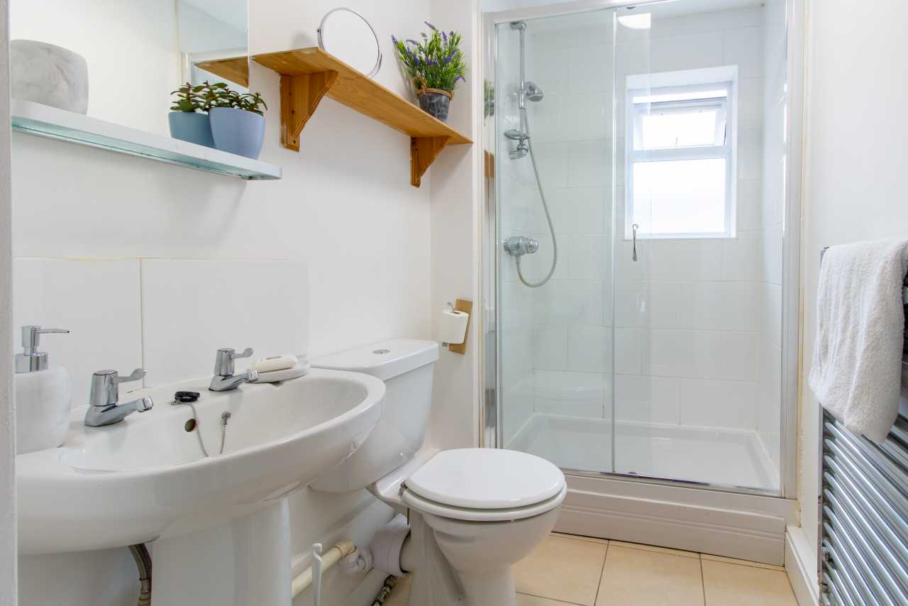 A bright bathroom with a double sink, toilet, glass shower enclosure, wall shelf and heated towel rail.