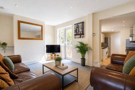 Furnished living room with leather sofas, television, large mirror, potted plant and an open doorway to the kitchen.