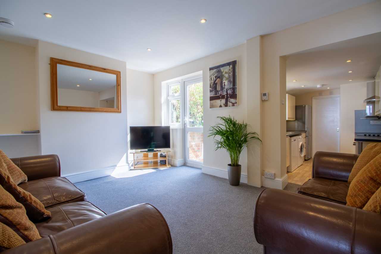 Furnished living room with leather sofas, television, large mirror, potted plant and an open doorway to the kitchen.