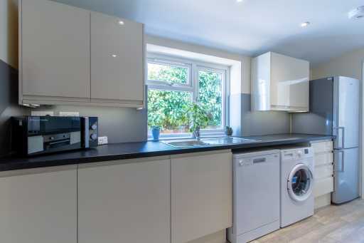 Modern fitted kitchen with pale cabinets, dark worktops, a window, sink, appliances and a refrigerator.