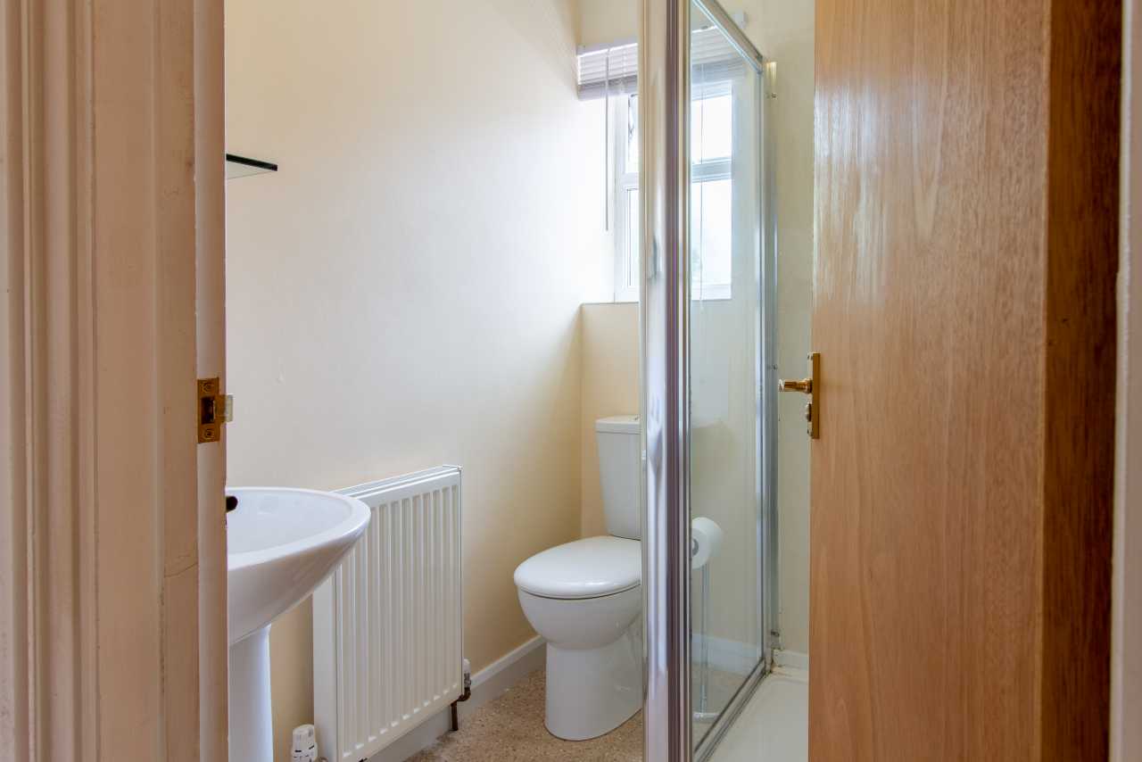 A small bathroom with a sink, toilet, shower enclosure, radiator and window.