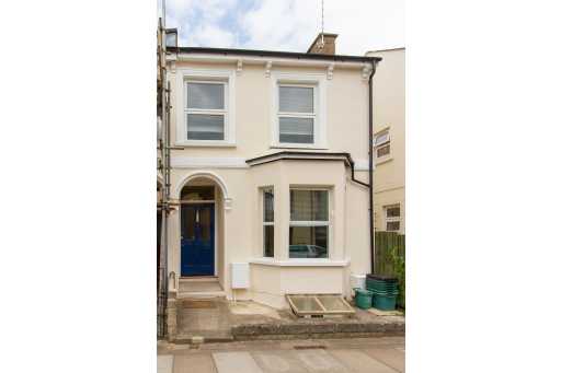 Front exterior of a narrow two-storey terraced house with cream walls, white-framed windows and a blue front door.