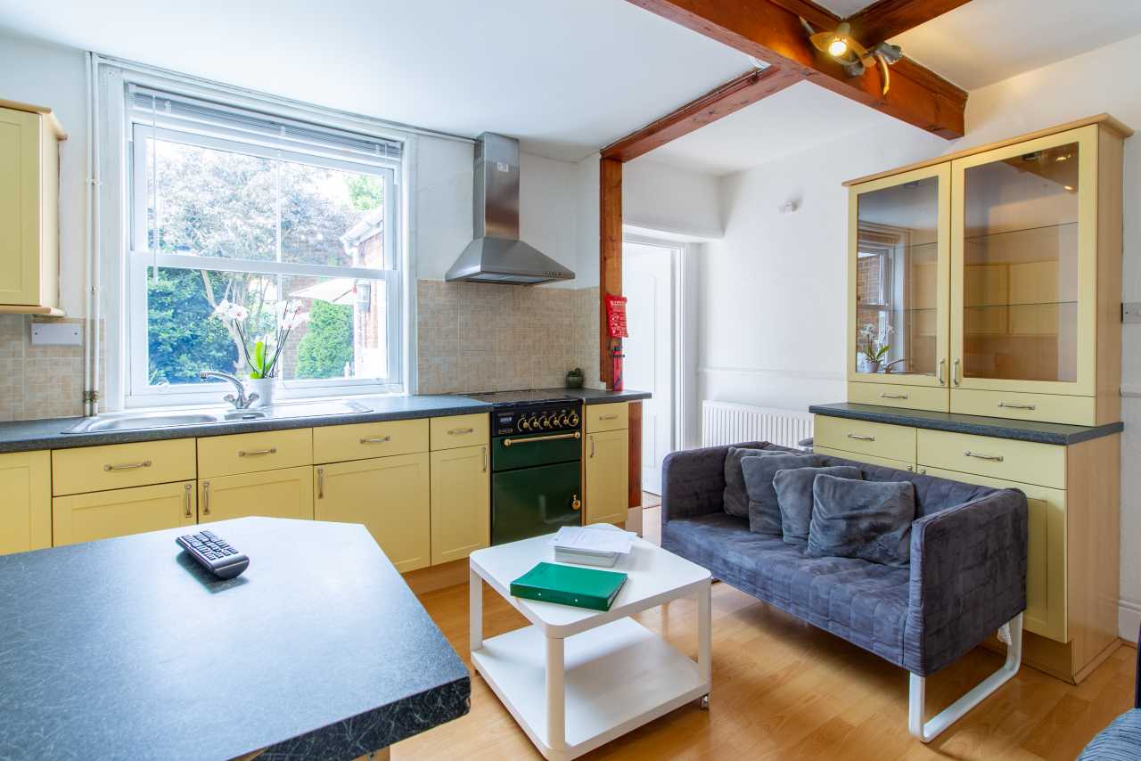 Open-plan kitchen and living area with yellow cabinets, cooker, dining island, sofa, coffee table and large window.
