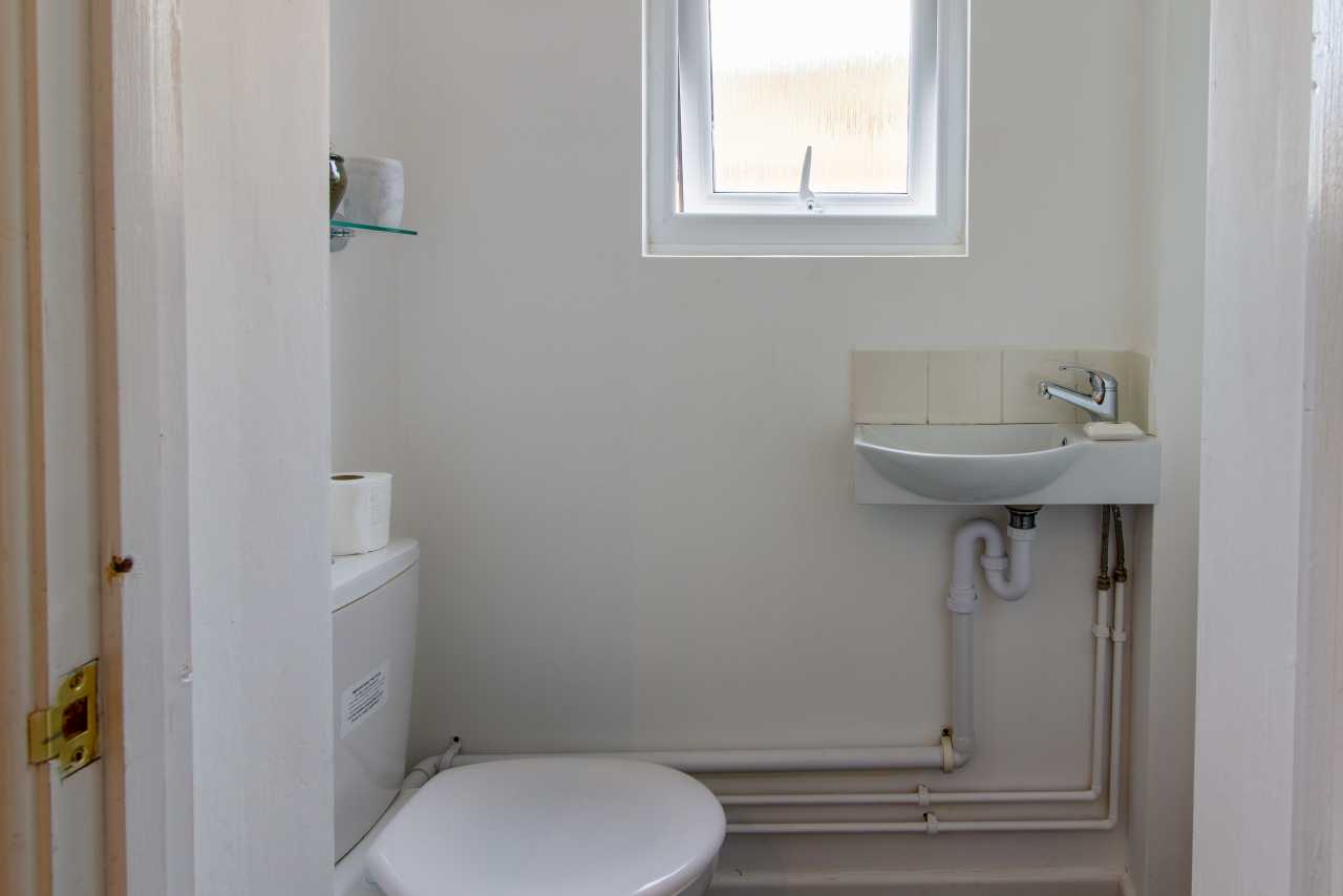 Small white bathroom with a toilet, wall-mounted sink, exposed pipes and a frosted window.