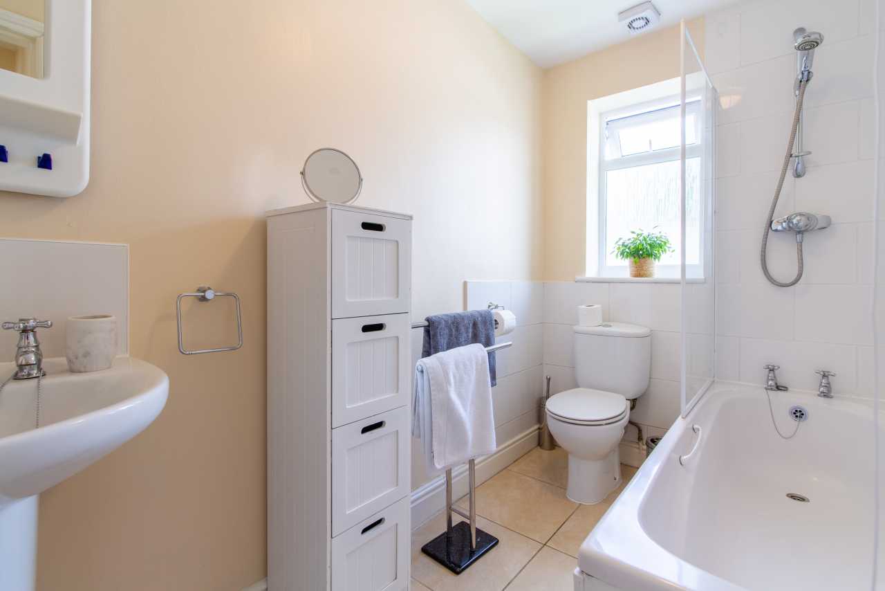 Bright bathroom with a bathtub, toilet, sink, storage cabinet, towel rack and window.