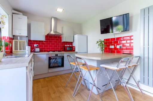 Bright open-plan kitchen and dining area with red tiled walls, white cabinets, a breakfast counter and folding chairs.