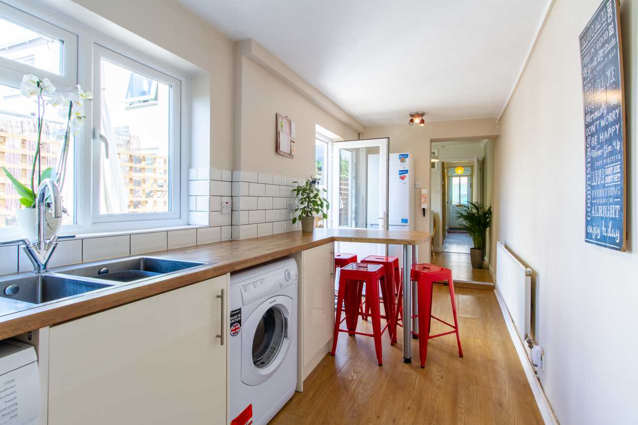 Bright shared kitchen and dining area with windows, appliances, a breakfast counter and red stools.