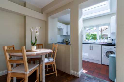 Dining area beside a bright kitchen with a table, chairs, cabinets, appliances and tiled flooring.