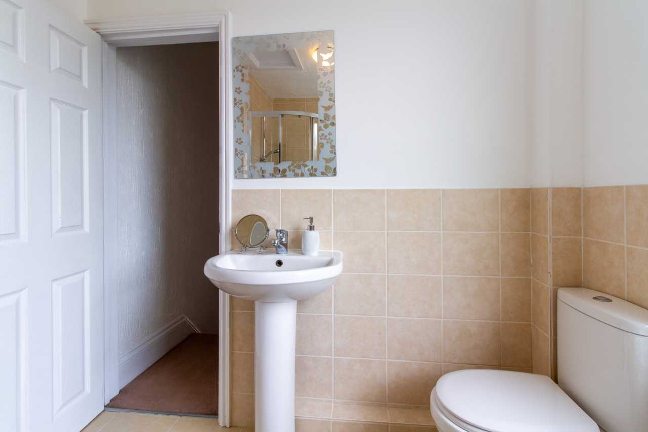 A small bathroom with a pedestal sink, toilet, tiled walls, mirror and open door.