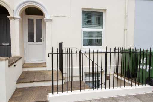 Front entrance of a terraced house with steps, railings, a window and wheelie bins.