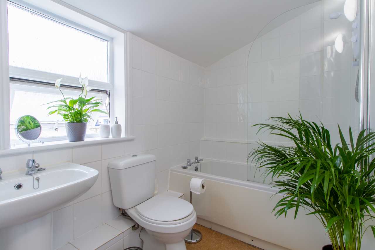 A bright tiled bathroom with a bathtub, toilet, sink, window, and potted plants.