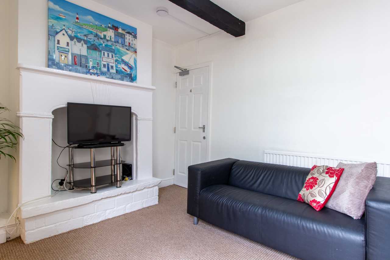Living room with a black sofa, television, white fireplace and colourful wall artwork.