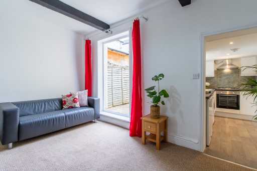 Bright living area with a blue sofa, red curtains, a small wooden side table and a doorway to the kitchen.