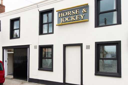 White two-storey building with black-framed windows, doors and a sign reading “HORSE & JOCKEY”.