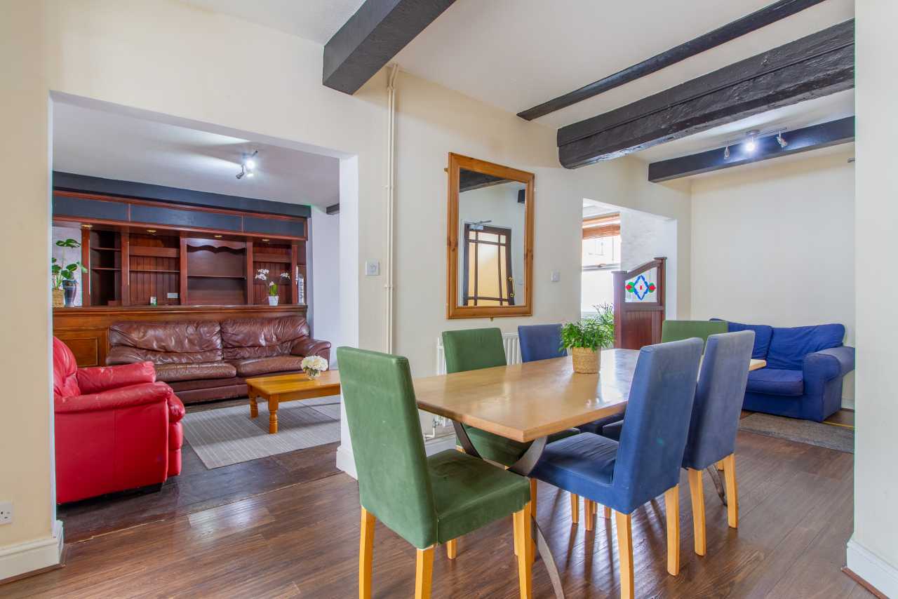 Dining and sitting area with a large table, upholstered chairs, sofas, exposed beams and wooden flooring.