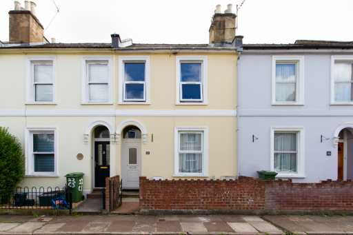 Row of attached terraced houses with painted facades, bay windows, front doors, chimneys and low brick walls.