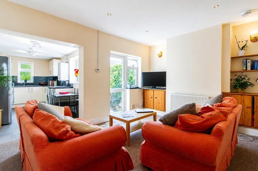A furnished living room with two orange sofas, a coffee table, television, radiator and shelving, opening into a kitchen and dining area.
