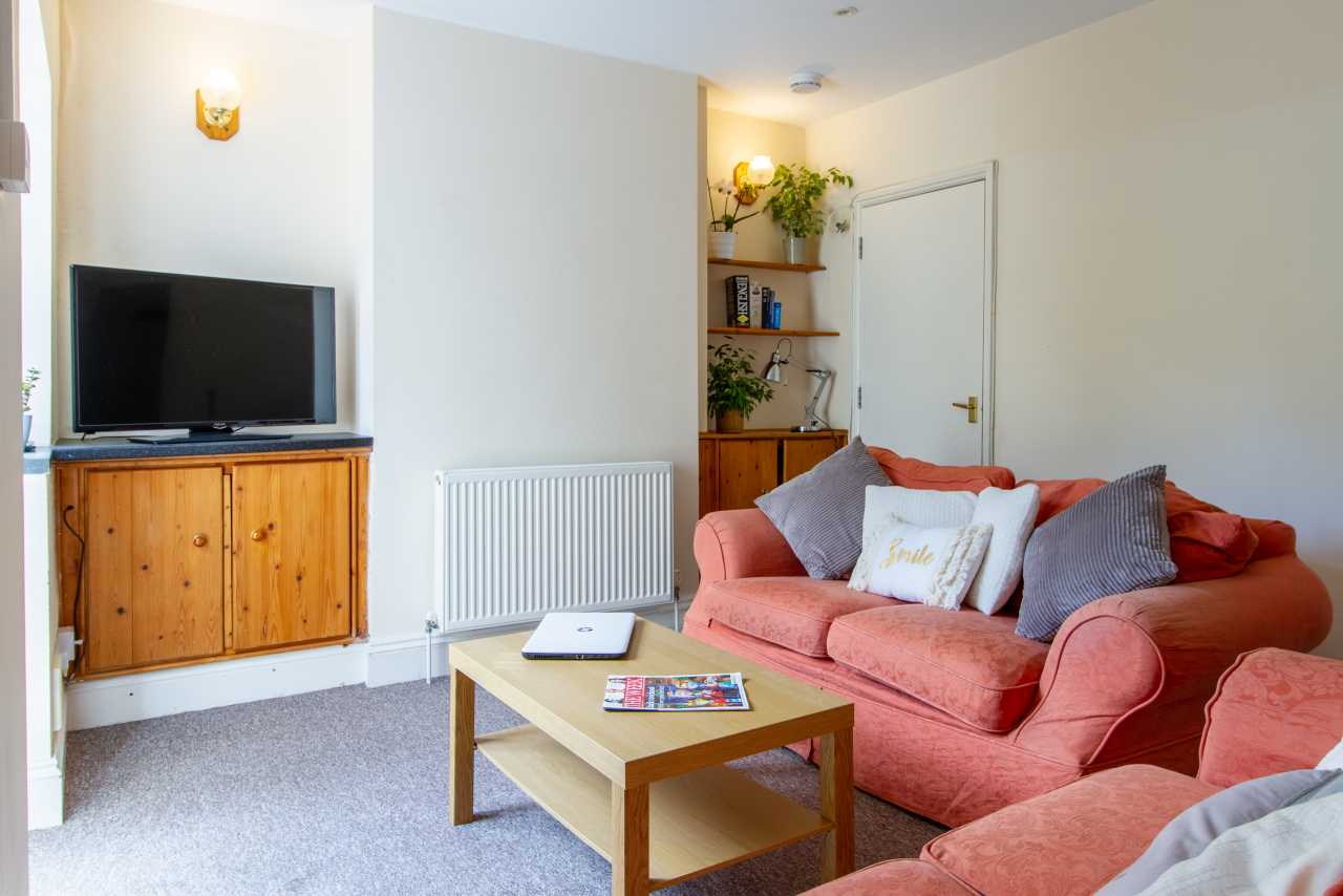 Furnished living room with a television, wooden cabinet, sofa, coffee table and radiator.