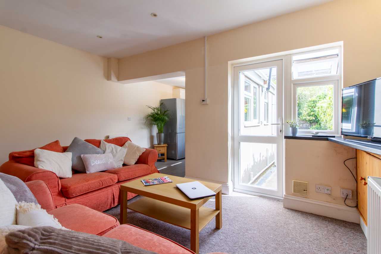 A furnished living room with red sofas, a coffee table, a television, and an open door to the outside.