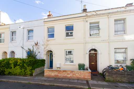 Row of attached terraced houses with cream façades, front doors, windows, small front gardens and bicycles.