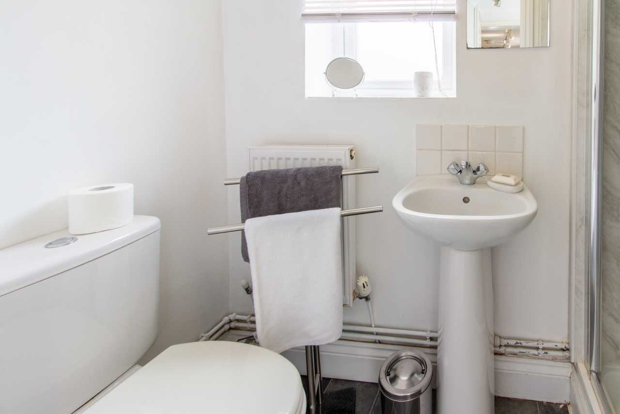 Small bathroom with a toilet, pedestal sink, towel rail, window and shower enclosure.