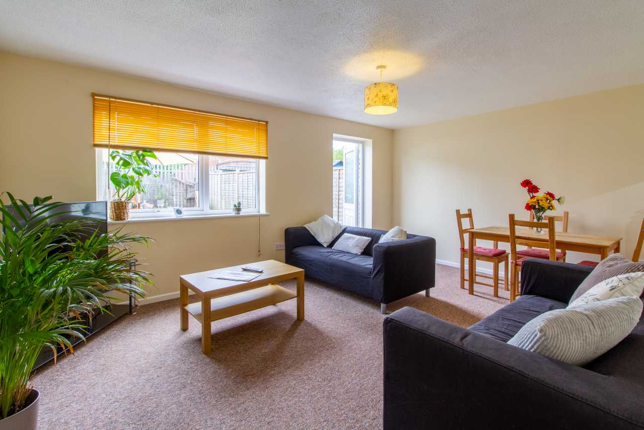 Living room with sofas, a coffee table, dining table and chairs, windows, and indoor plants.