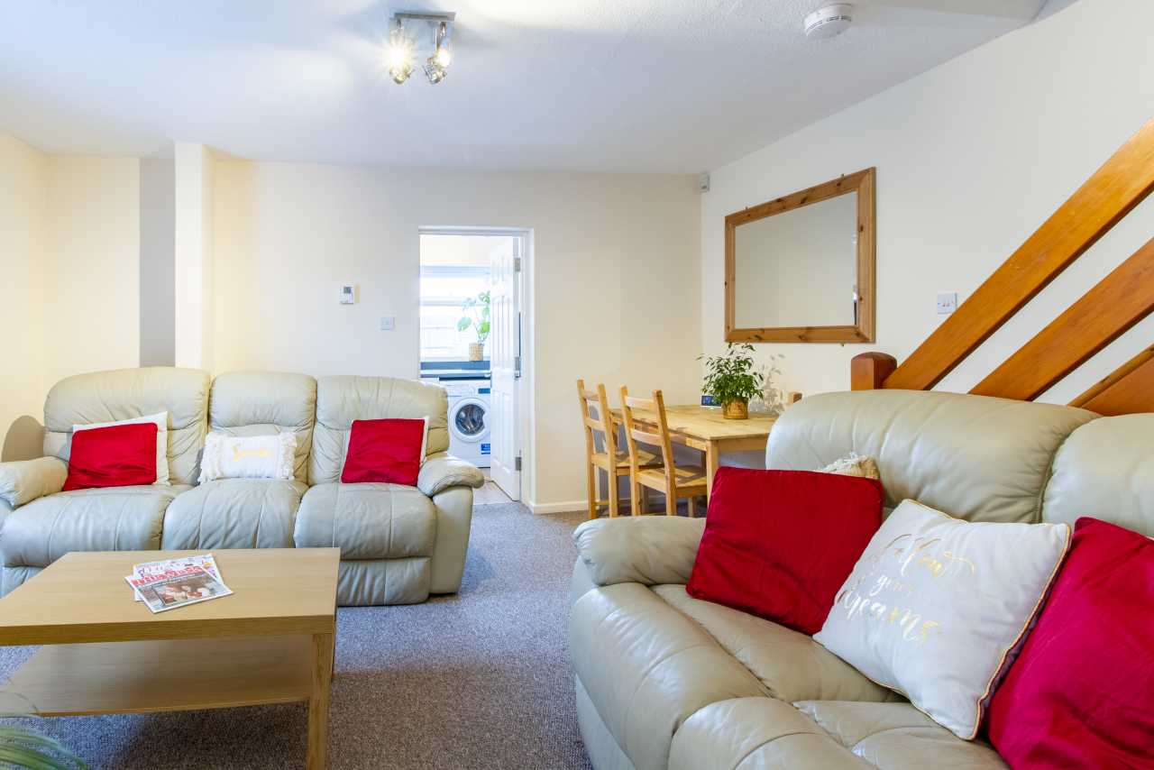 Bright shared living and dining room with sofas, red cushions, a coffee table, dining table and staircase.