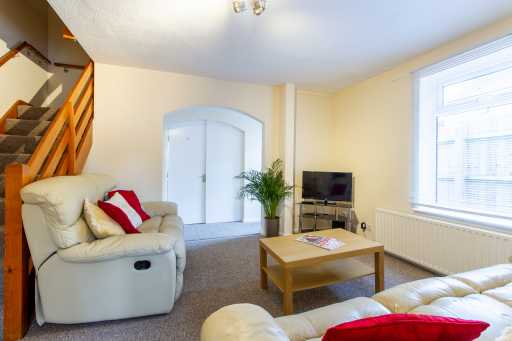 A furnished living room with sofas, a coffee table, television, radiator, window and staircase.