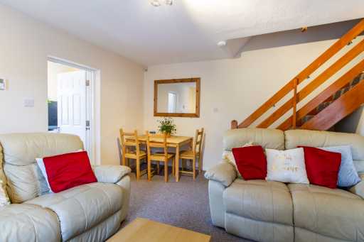 Living room and dining area with sofas, a dining table, and a wooden staircase.