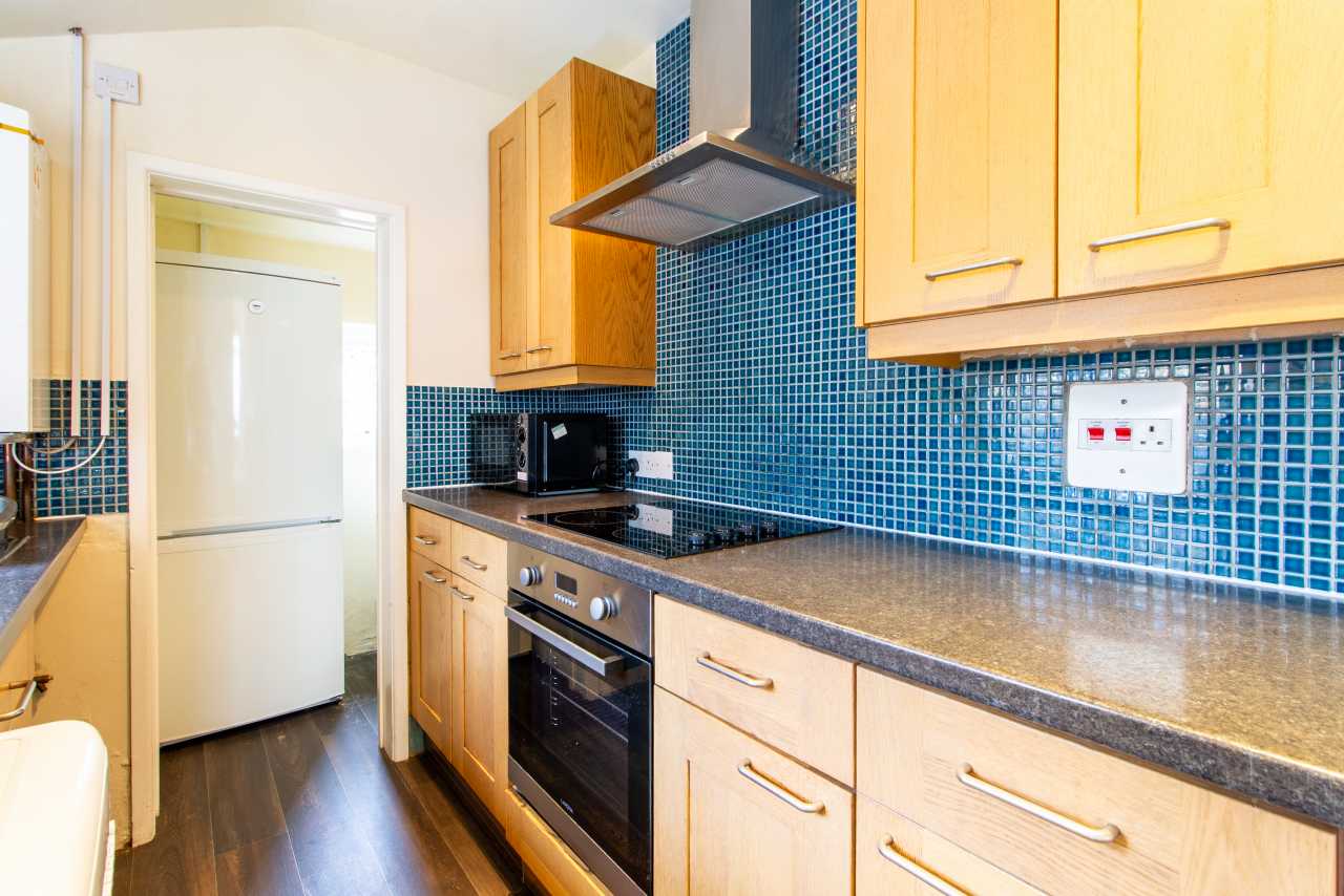 Bright fitted kitchen with wooden cabinets, dark worktops, blue mosaic backsplash, oven, hob and refrigerator.
