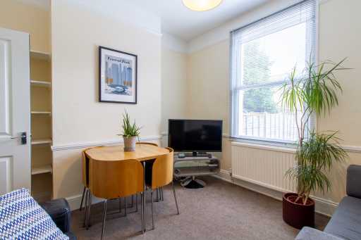 Furnished living room with a dining table, television, sofa, plants and a large window with blinds.