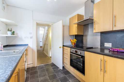 Bright fitted kitchen with wooden cabinets, dark countertops, built-in oven and tiled floor.