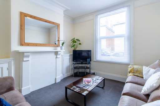 A furnished living room with a fireplace, wall mirror, television, coffee table, armchairs and sofa.