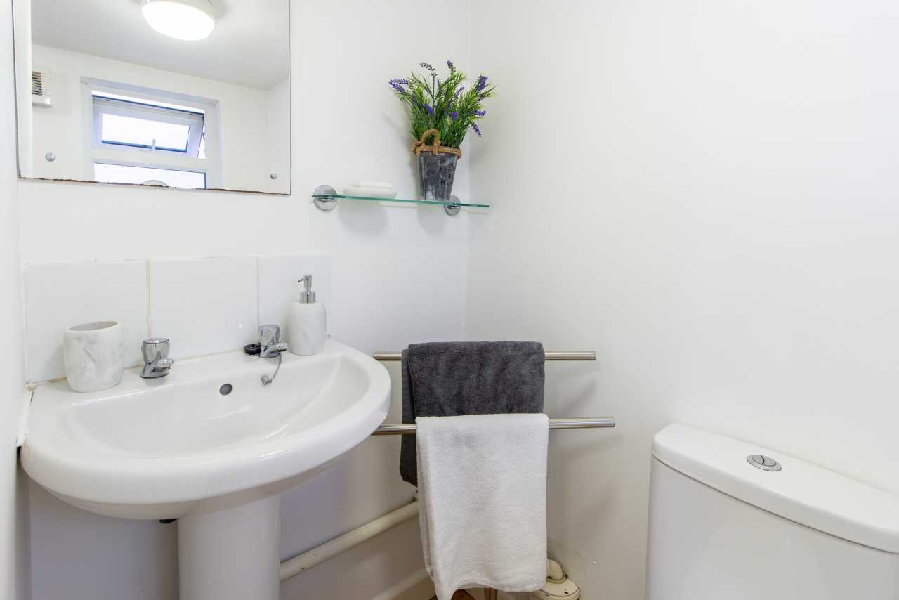A bright bathroom with a washbasin, mirror, towels on rails, toilet and a small vase of flowers.