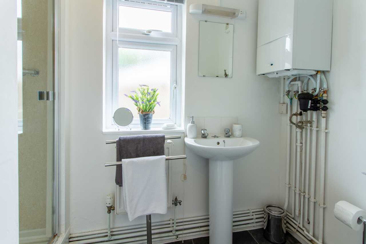 Bright bathroom with a pedestal sink, mirrored cabinet, shower enclosure, towel rail, toilet roll holder and wall-mounted boiler.