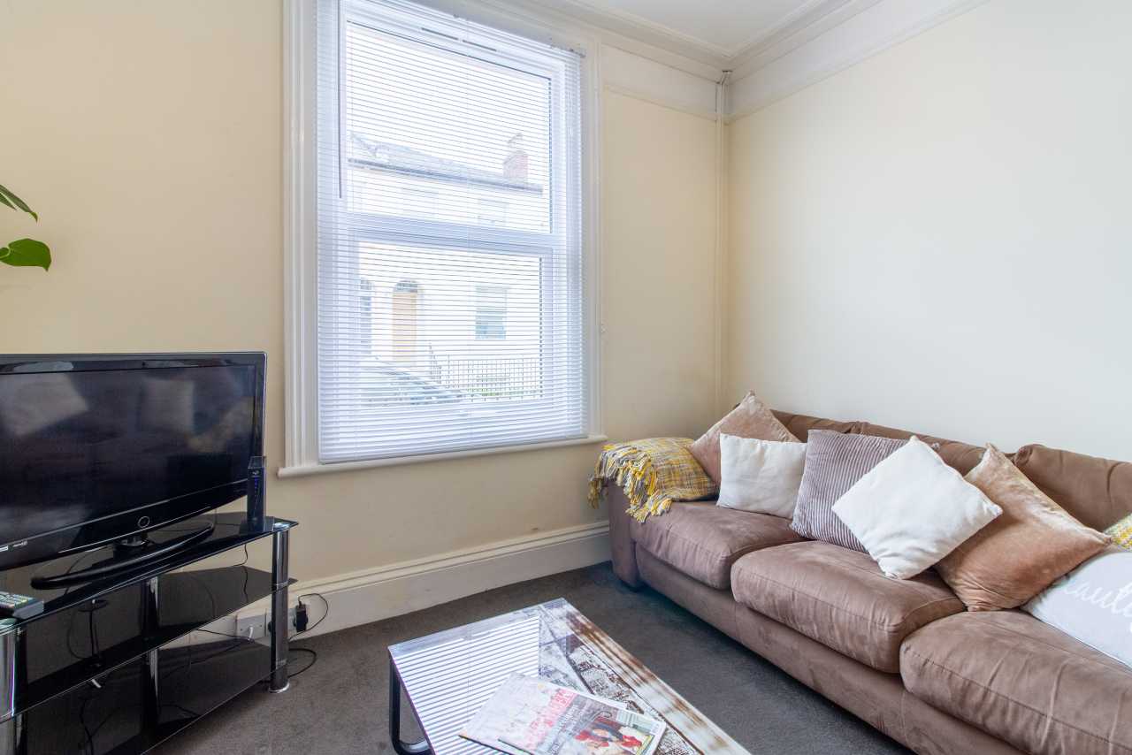 Living room with a television, sofa, cushions, coffee table and a window with blinds.