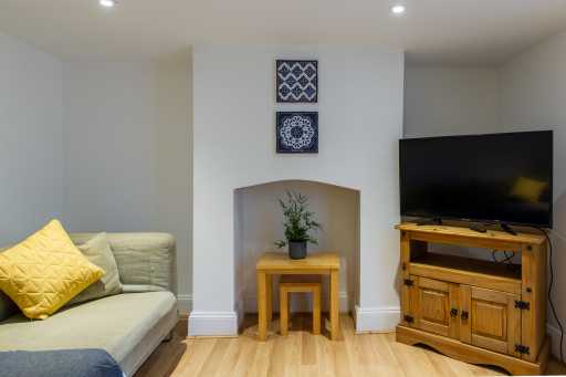 Living room with a sofa, yellow cushions, a television on a wooden cabinet, and a small table with a plant.