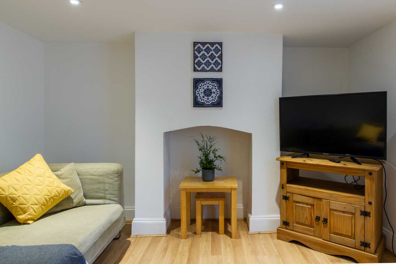 Living room with a sofa, yellow cushions, a television on a wooden cabinet, and a small table with a plant.