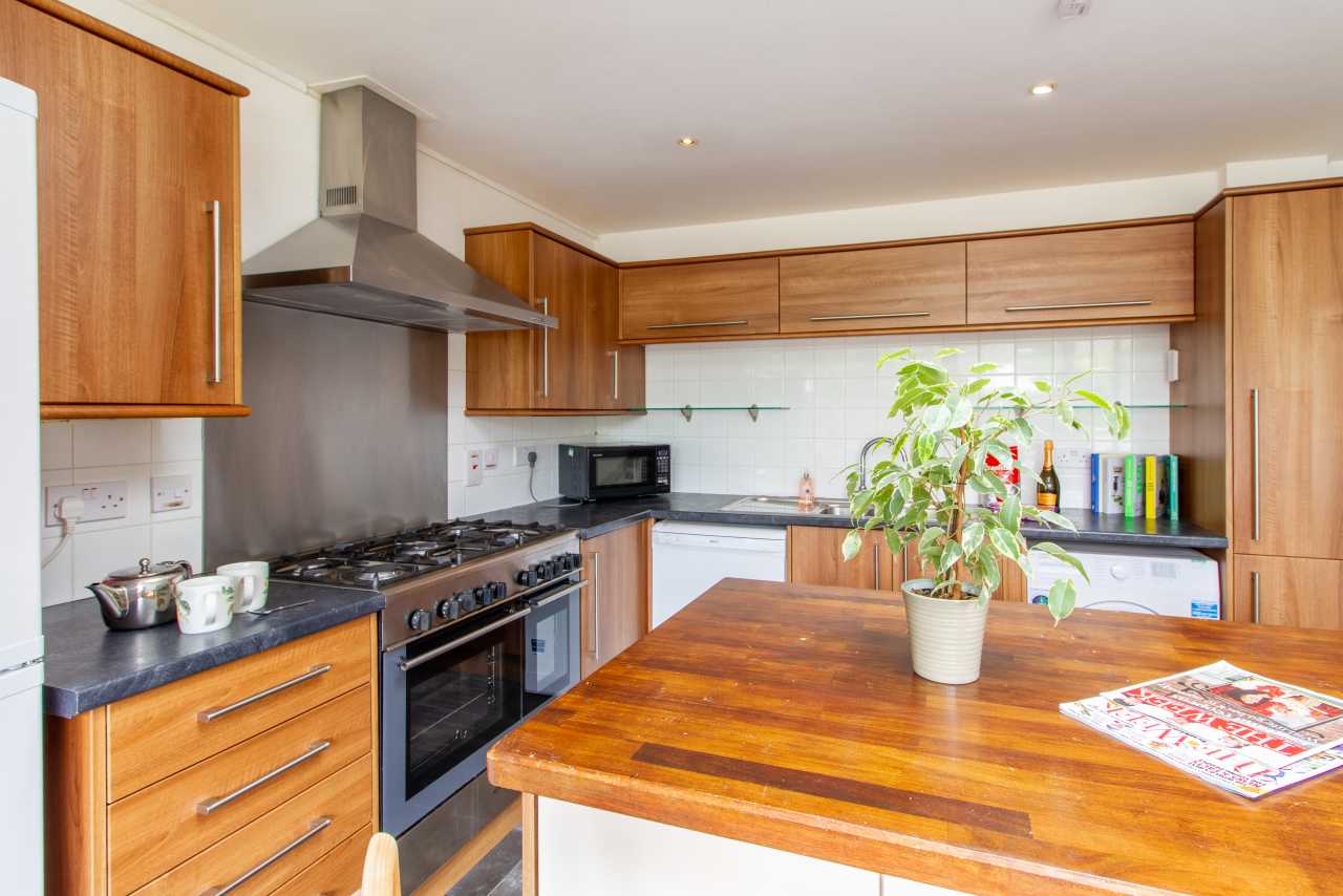 Bright fitted kitchen with wooden cabinets, a large range cooker, tiled splashback, and a central wooden island.