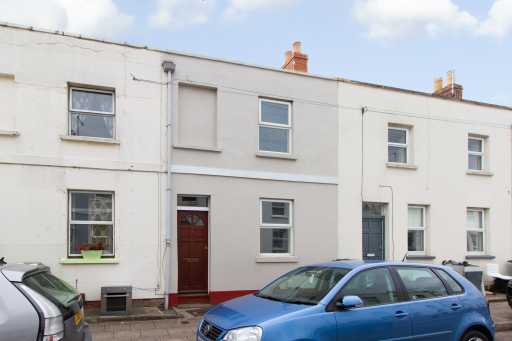 Street-facing row of attached residential houses with doors, windows, parked cars and chimneys.