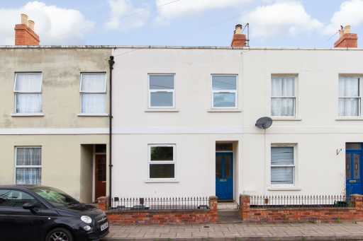 Street view of a row of attached terraced houses with brick chimneys, front doors, windows, railings and a parked car.