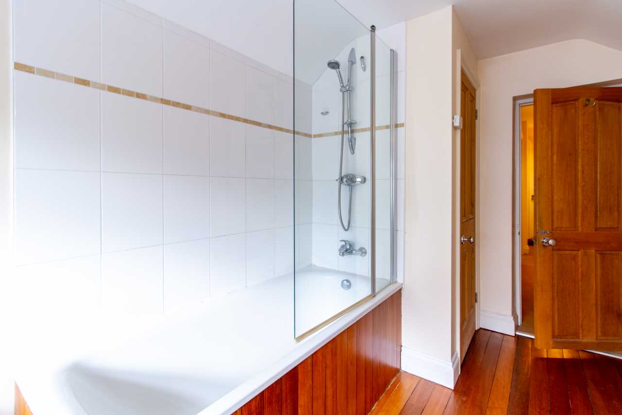 A tiled bathroom with a bathtub, glass shower screen, shower fixtures, wooden wall panels, and a wooden door.