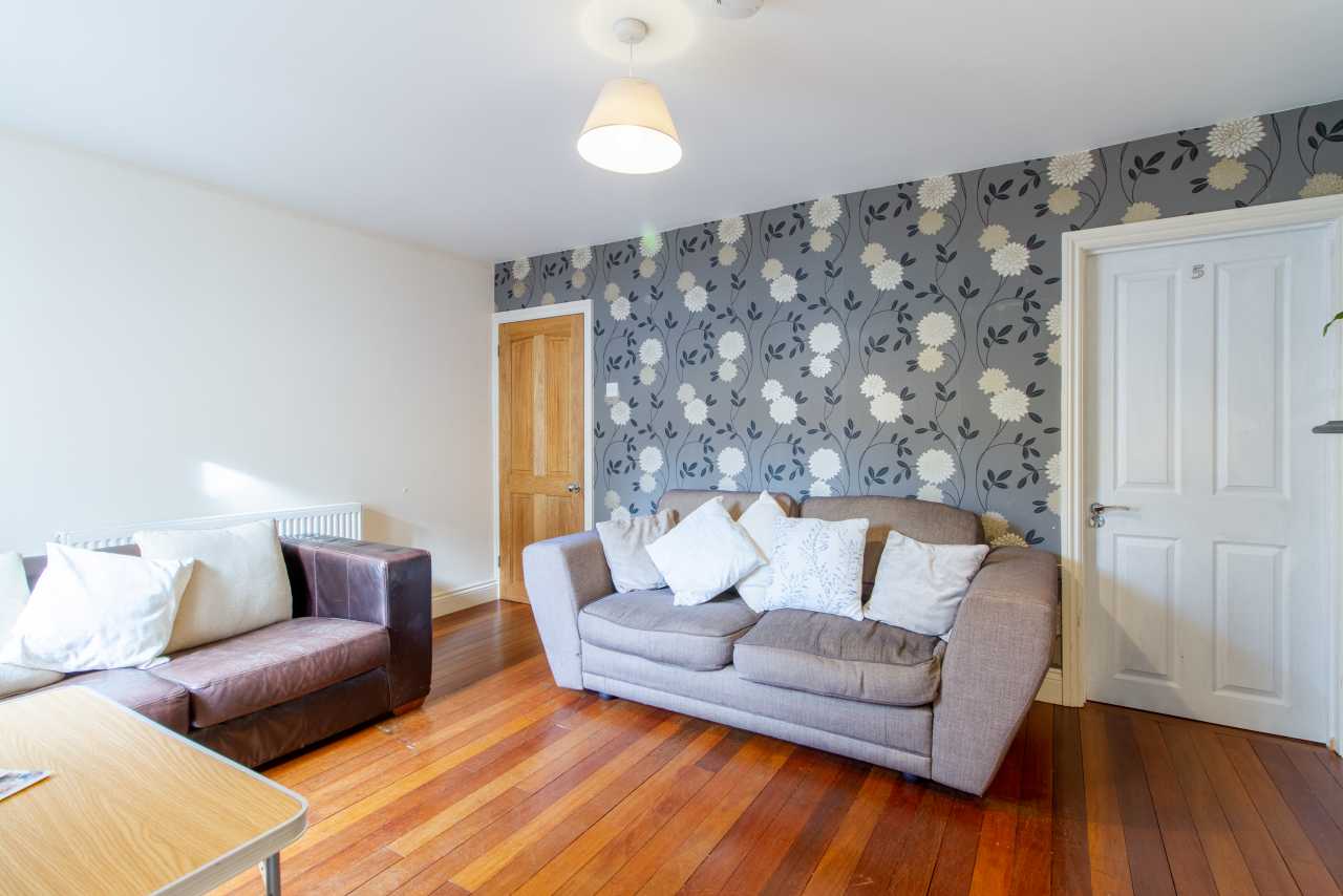 Furnished living room with sofas, patterned wallpaper, wooden flooring, and two doors.