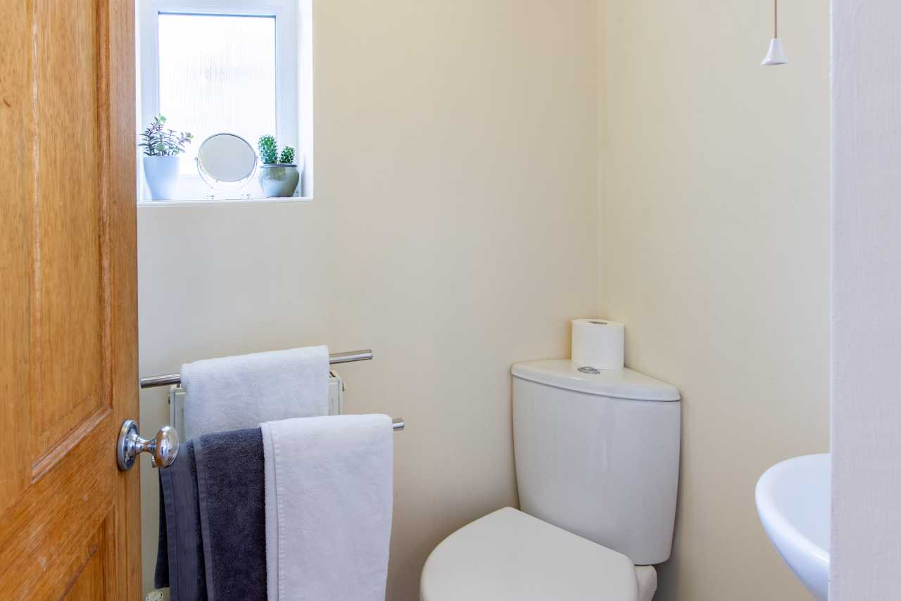 Small bathroom with a toilet, sink, towel rail, window and wooden door.