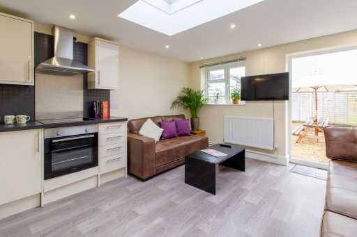 Open-plan living area with a fitted kitchen, sofa, coffee table, television and skylight.