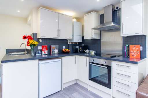 Bright modern fitted kitchen with white cabinets, dark countertops, sink, oven, hob, extractor hood and a small dining area.